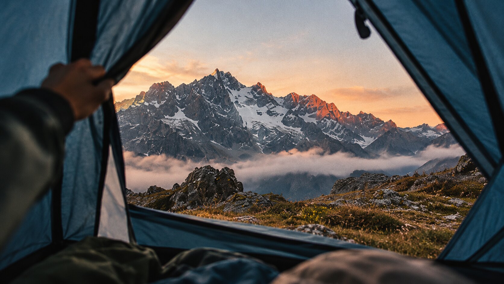 HIKING CLUB: Blick aus dem Zelteingang auf einen leuchtenden Berggipfel bei Sonnenaufgang