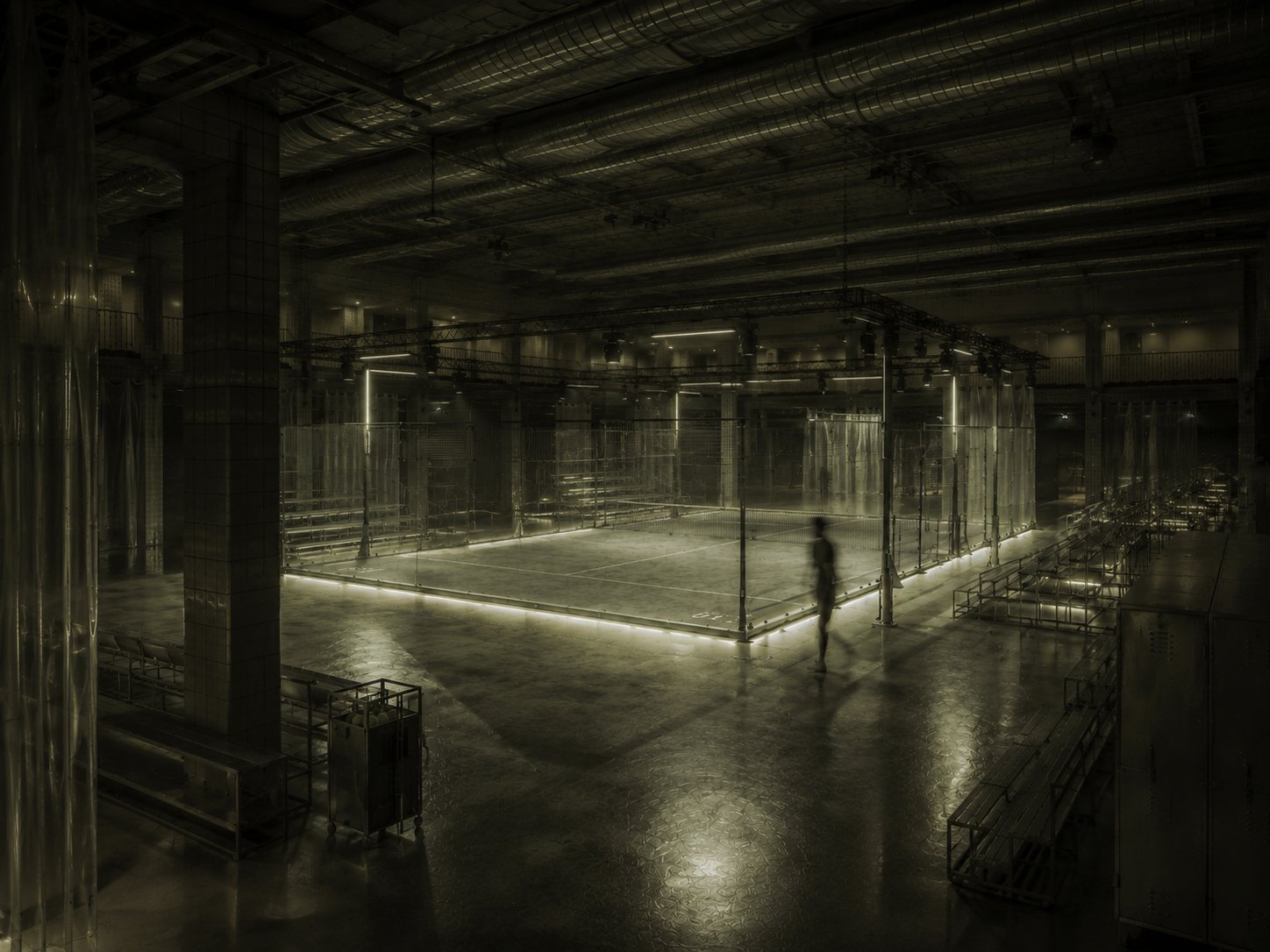 Padel Court: glass court with a line of light in a dark industrial hall, a figure walking past